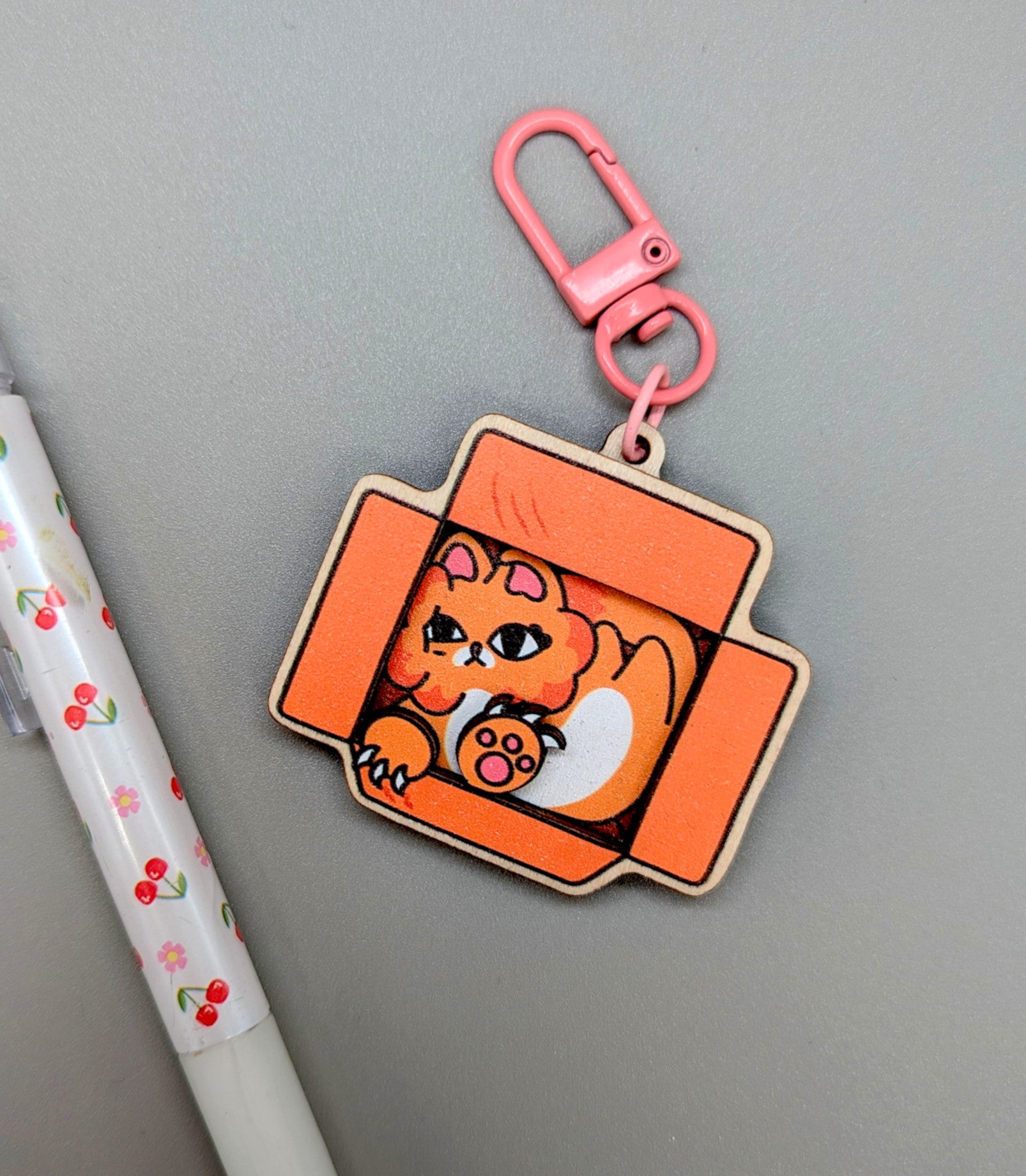 Keychain with a cat design on an orange background, attached to a pink carabiner.