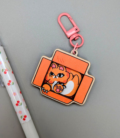 Keychain with a cat design on an orange background, attached to a pink carabiner.