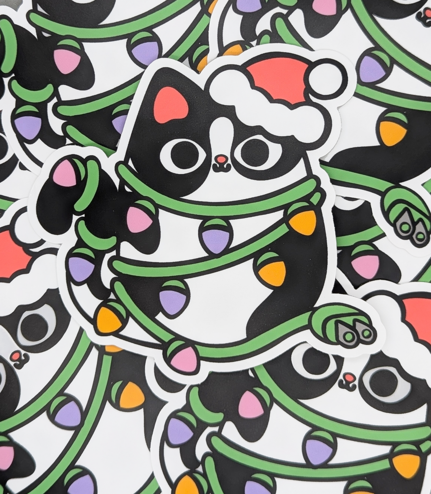 Sticker of a cat wrapped in Christmas lights with a Santa hat on a white background.