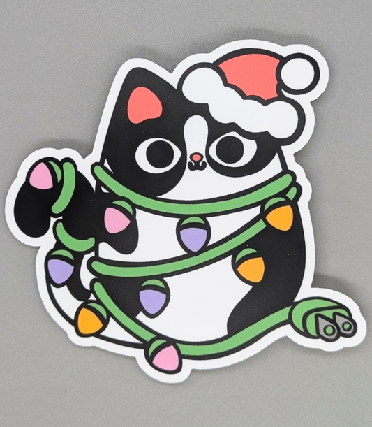 Sticker of a black cat with a Santa hat and Christmas lights on a gray background