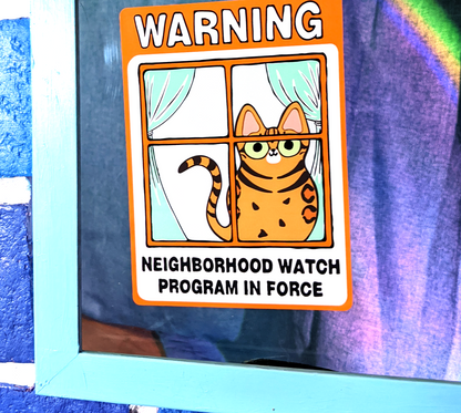 Cartoon bengal cat window cling on a window that says warning: neighborhood watch program in force. Drawing is of a happy bengal cat.