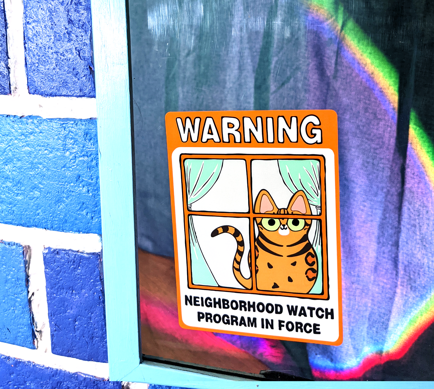 Neighborhood watch cat sticker with happy bengal cat is displayed on a window. Cute bengal cat watches passersby 