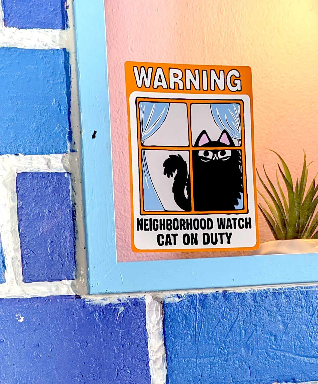 Cartoon fluffy black cat watches from window. Window cling says Warning: Neighborhood Watch Cat on Duty