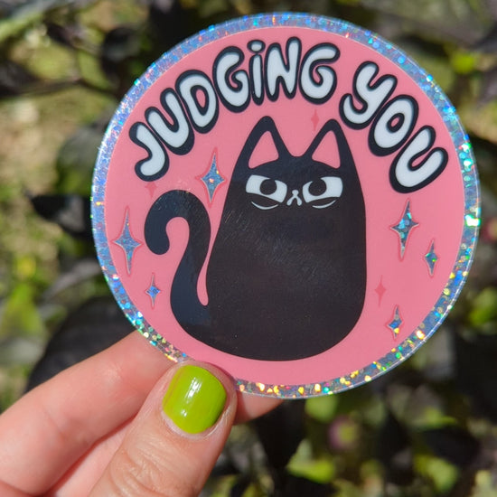 Glitter sticker of judgy angry black cat shines in the sun, each movements sparkles