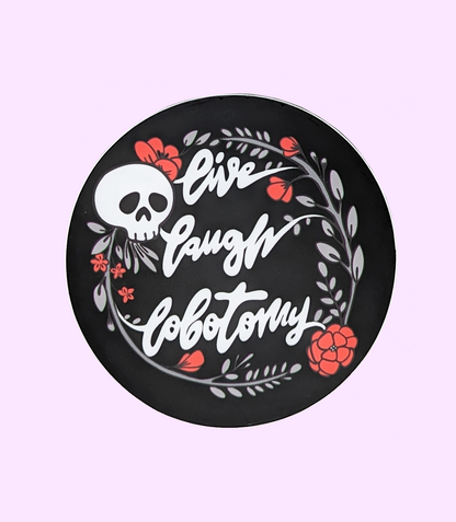 Live Laugh Lobotomy Circle Vinyl Sticker. Sticker says "Live, Laugh, Lobotomy" and features a skull and flowers design.